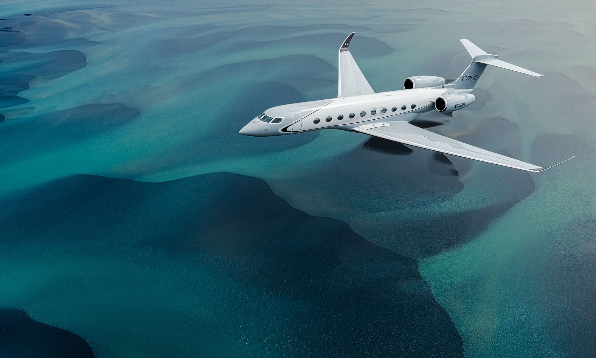 Gulfstream G700 flying low over turquoise water